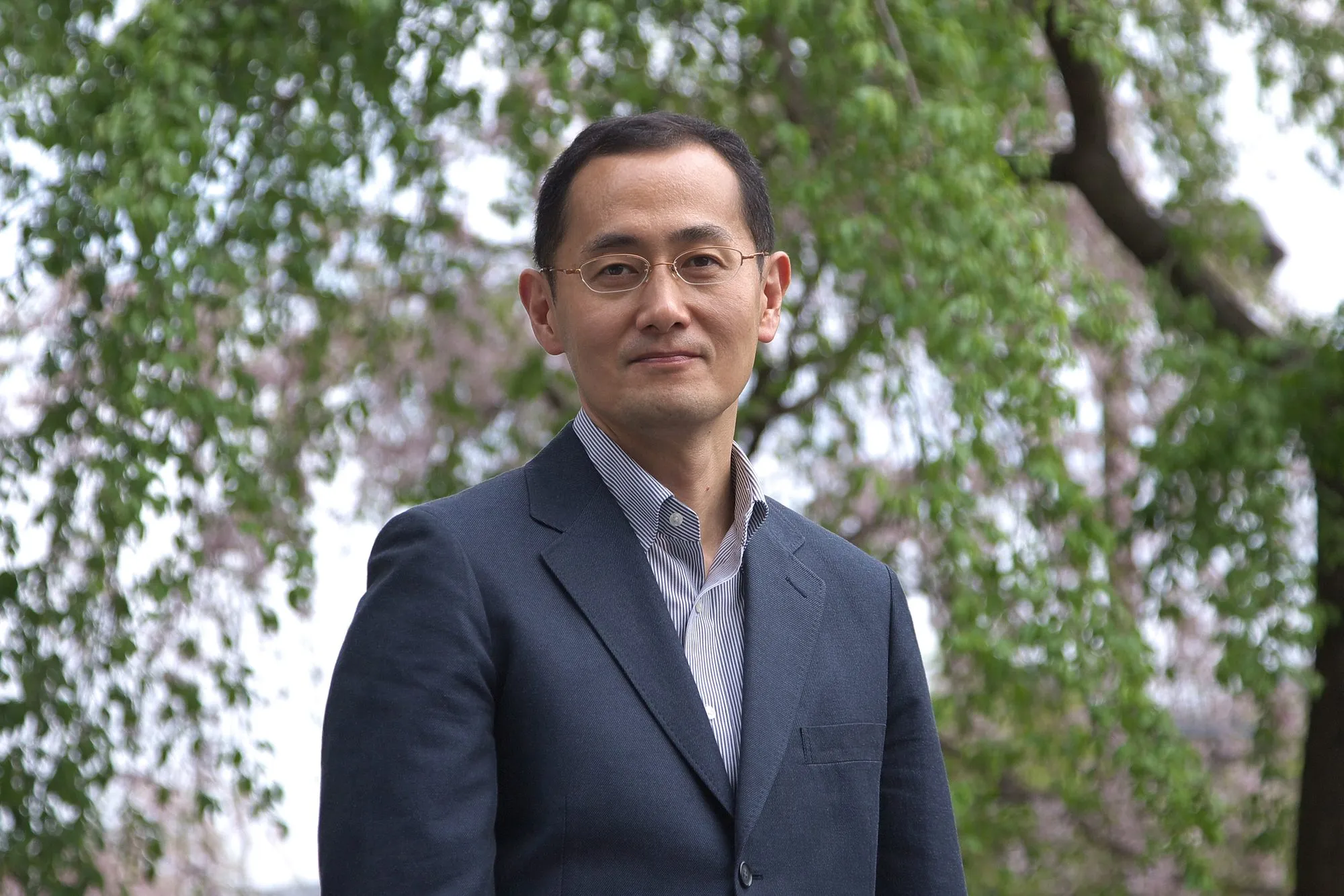 Shinya Yamanaka in a navy jacket, standing outdoors in front of a leafy tree.
