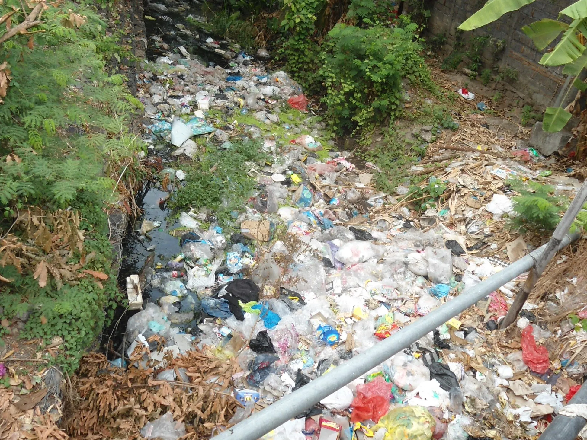 Botigues de plàstic, bosses i embolcalls ofegant un llit estret al costat d'un jardí a Bali.