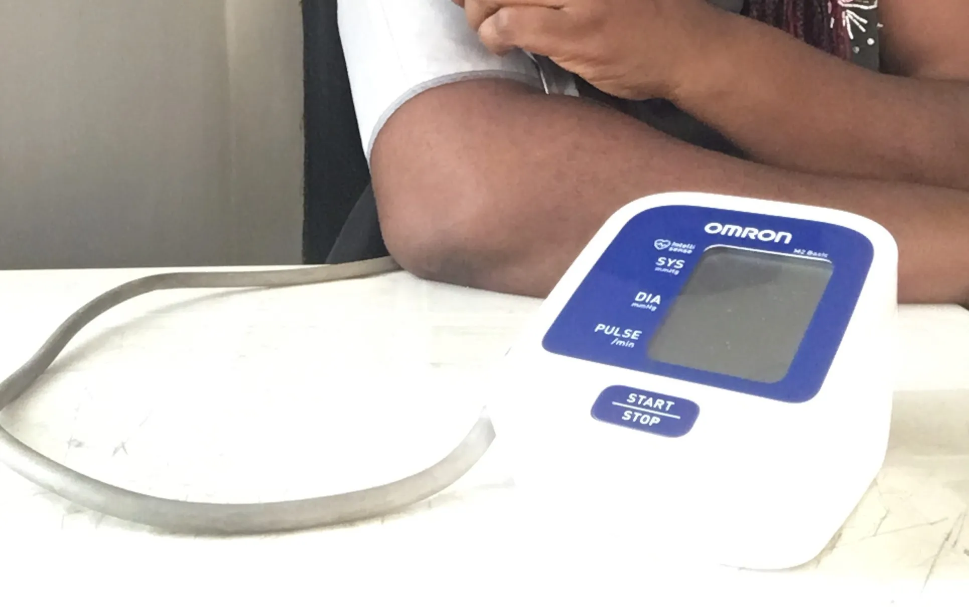 A person's upper arm in an inflatable cuff connected to an automatic blood pressure monitor on a table.