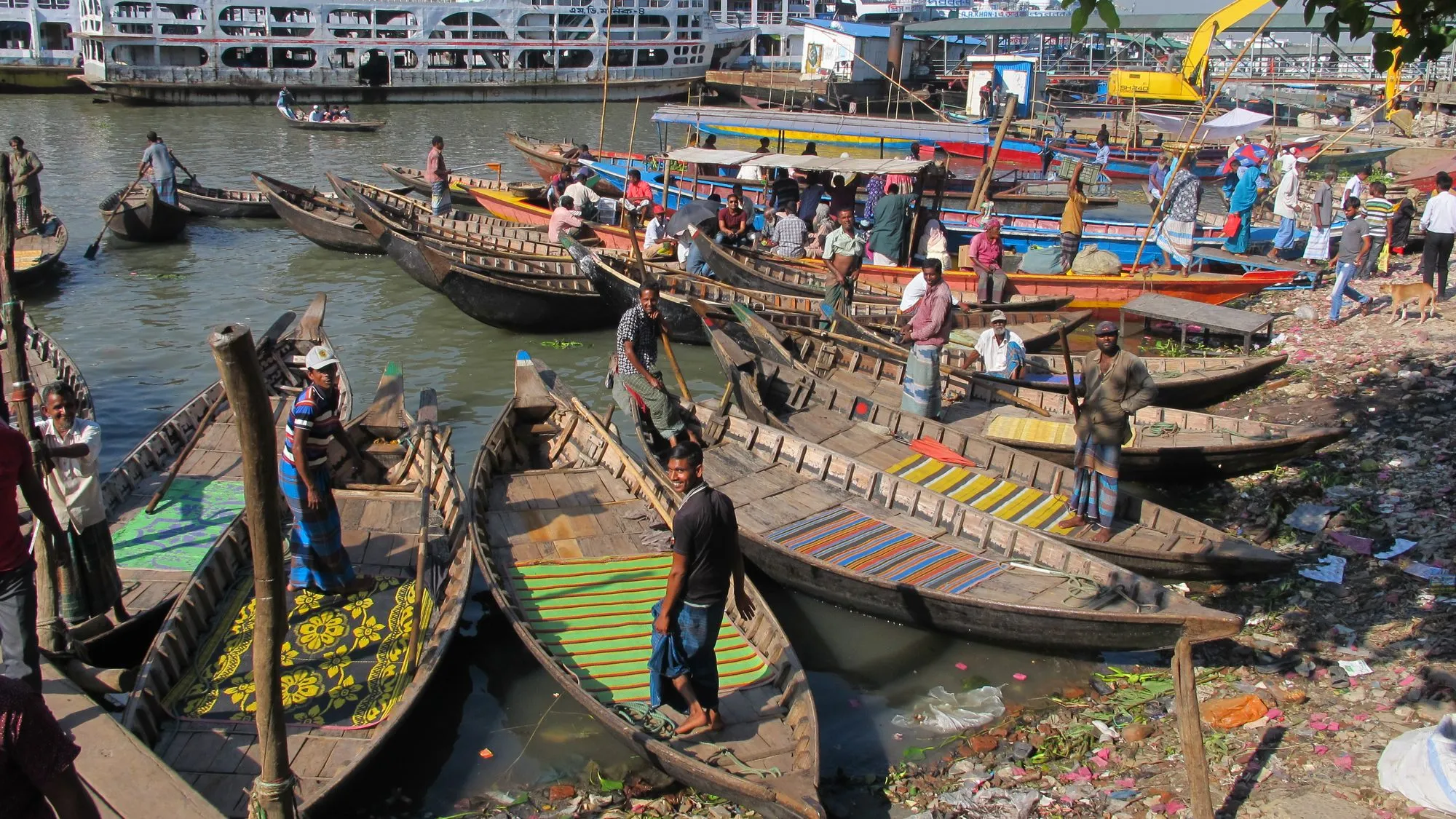 Vaixells de fusta de passatgers a la vora del port fluvial de Sadarghat al Buriganga, a Dhaka, amb escombraries al llarg de la riba.
