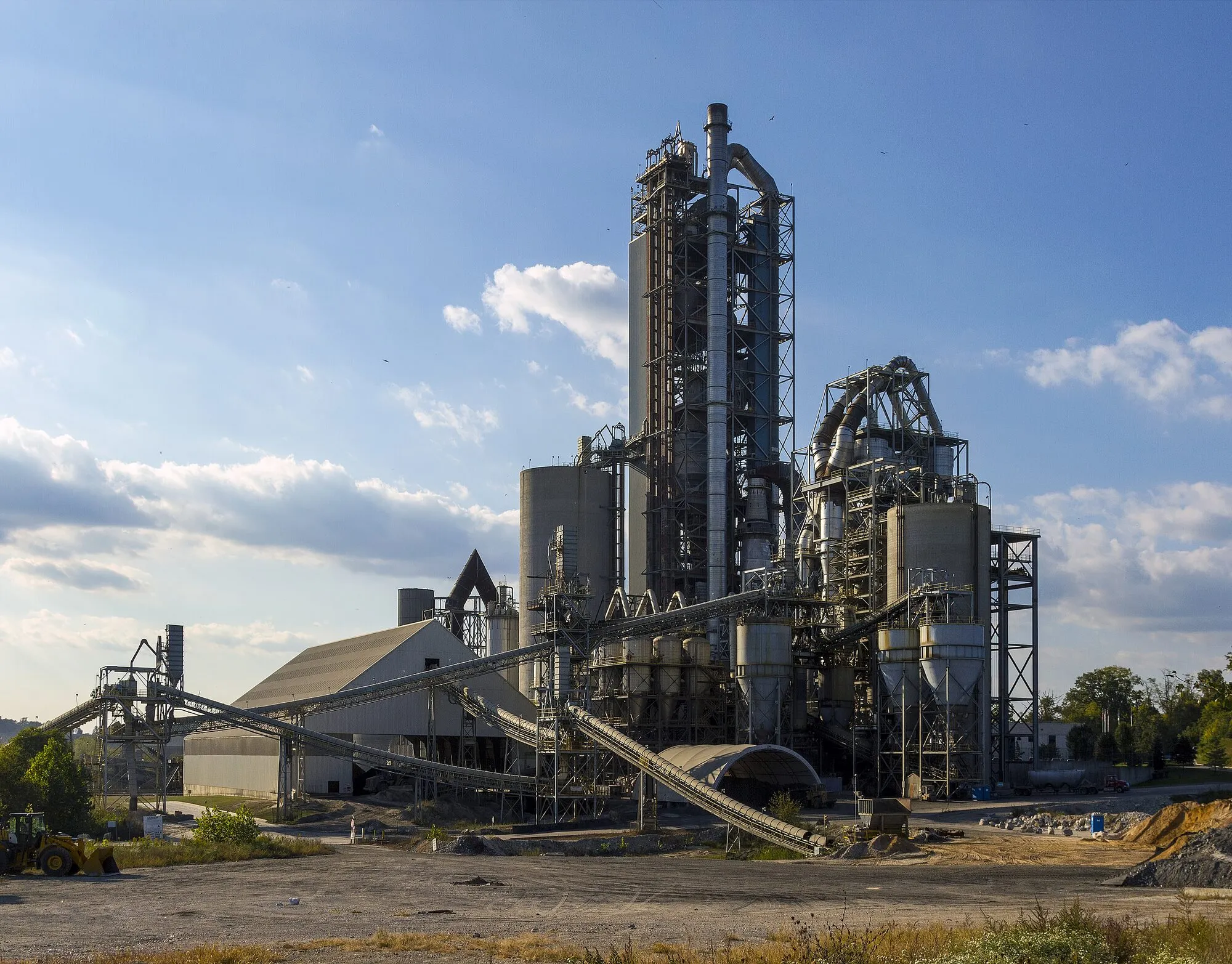 A tall cement plant tower of steel and concrete under a blue sky.
