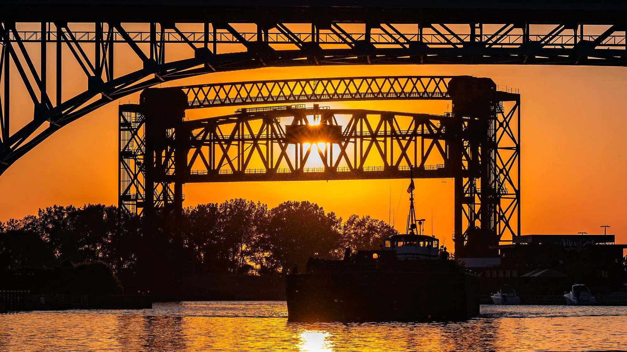 A steel lift bridge silhueted against an orange sunset over the Cuyahoga River in Cleveland.