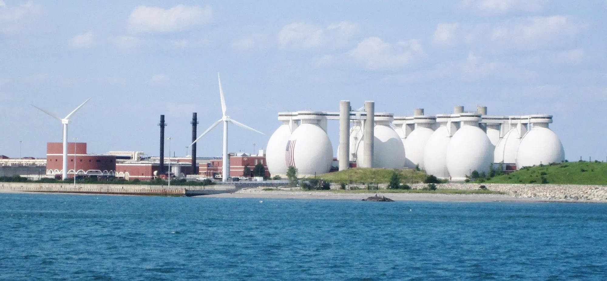 The egg-shaped sludge digesters and wind turbines of the Deer Island treatment plant, seen across the blue water of Boston Harbor.