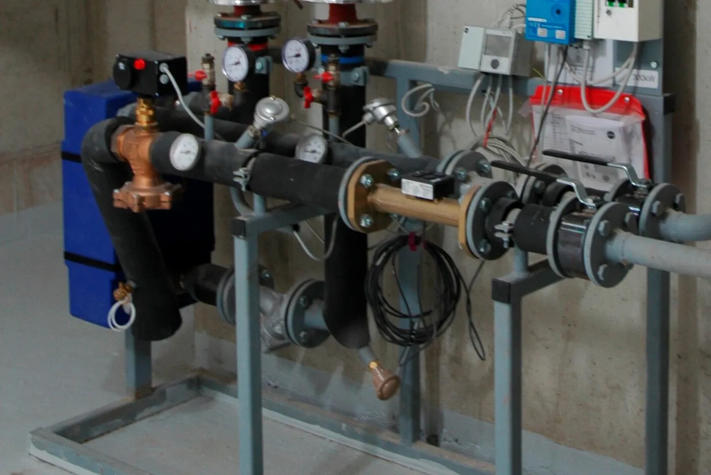 A compact district heating transfer station with a blue plate heat exchanger, pumps, valves and gauges.