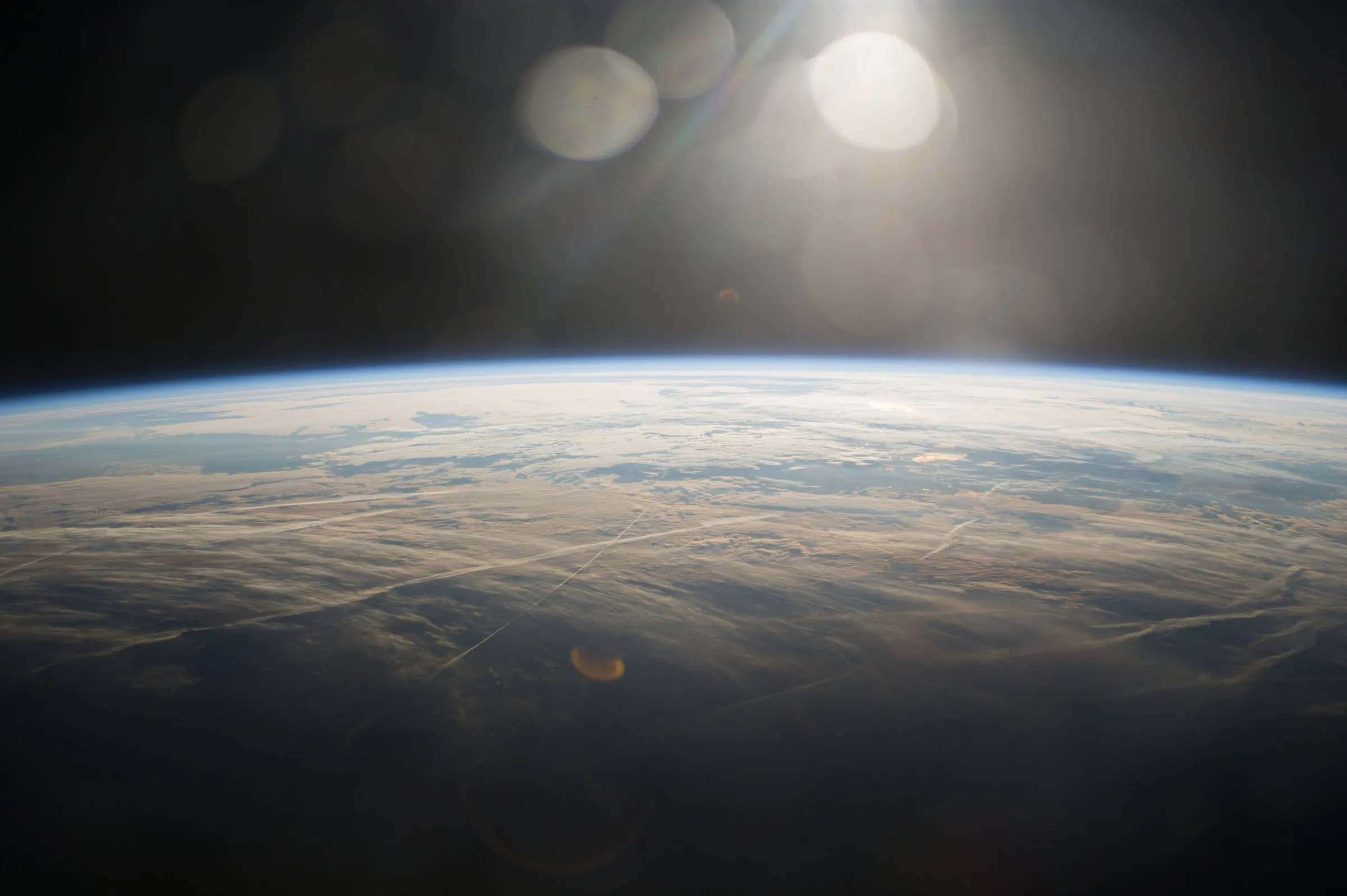 Sunce sjaji iznad zakrivljenog plavog ruba Zemlje, s tankim slojem atmosfere iznad oblaka, viđeno sa Međunarodne svemirske postaje.