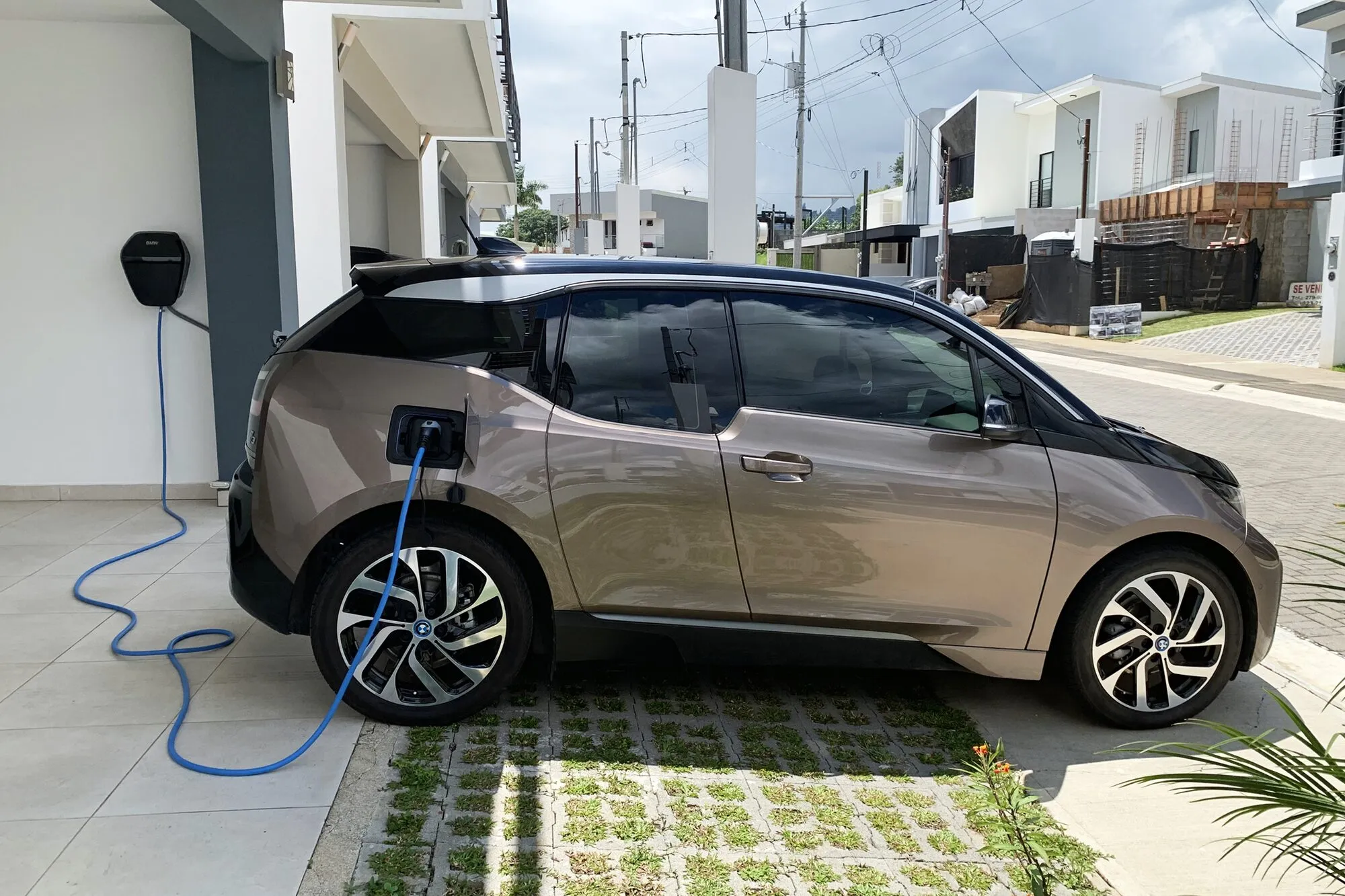A small electric car plugged into a wall charger in front of a modern house.