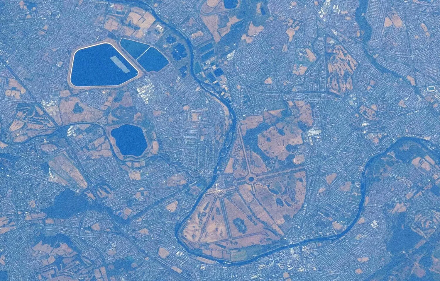 A satellite-style view from space of west London: two large reservoirs, one with a thin grey strip of floating panels, the winding River Thames and Bushy Park.