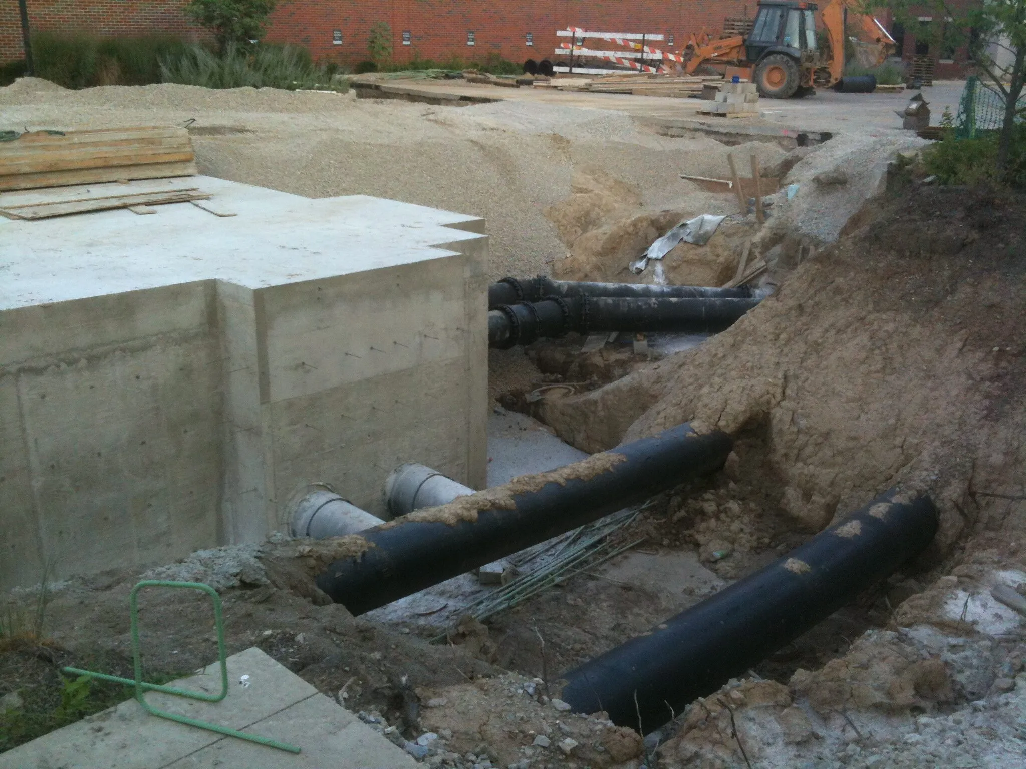 Large black plastic pipes being laid in a trench beside a concrete chamber on a construction site.