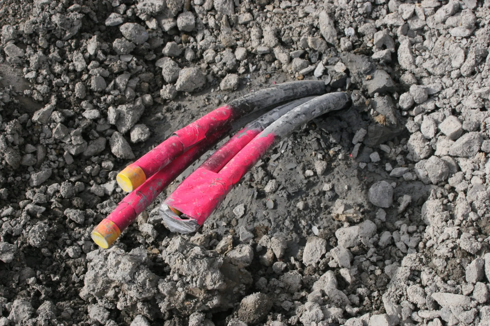 The top ends of a borehole heat exchanger: two pairs of plastic pipes, capped in red, sticking out of gravel.