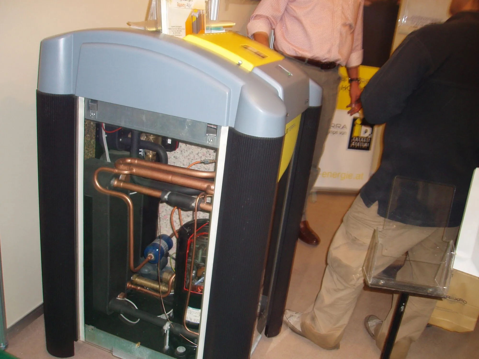 A floor-standing heat pump with its front casing removed, showing copper pipes, a compressor and a pump inside.