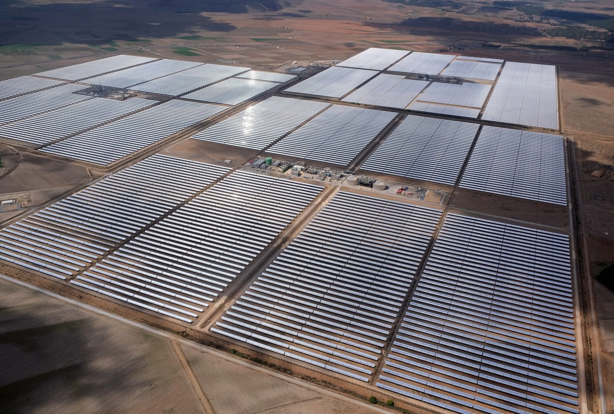 Aerial view of long rows of curved mirrors in large rectangular fields on a dry plain in southern Spain.