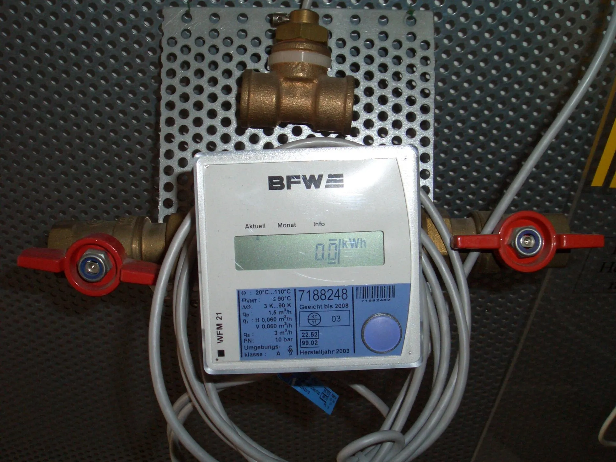 An electronic heat meter with a small digital display, mounted between two pipe valves.
