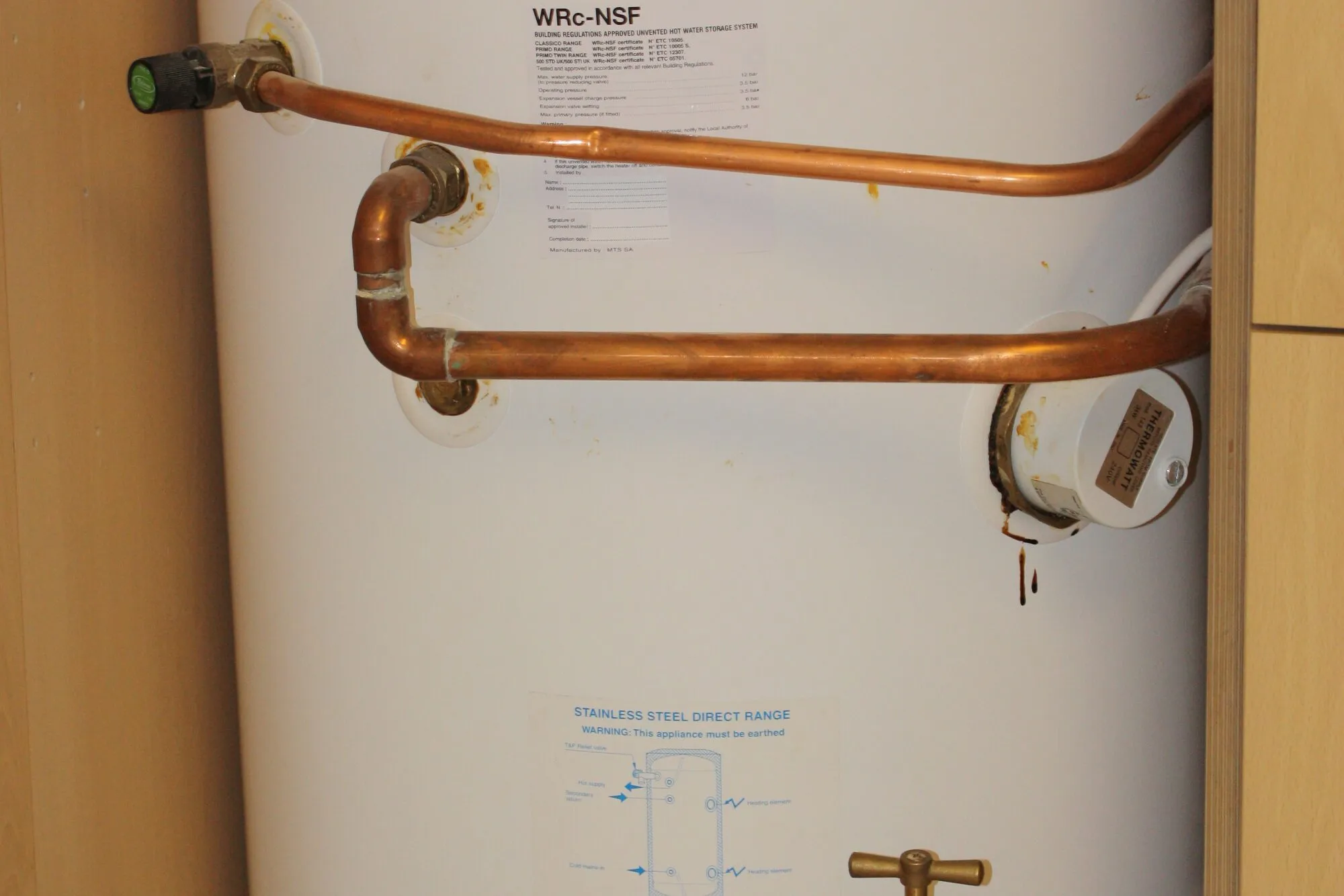 A white hot-water cylinder with copper pipes in a cupboard.