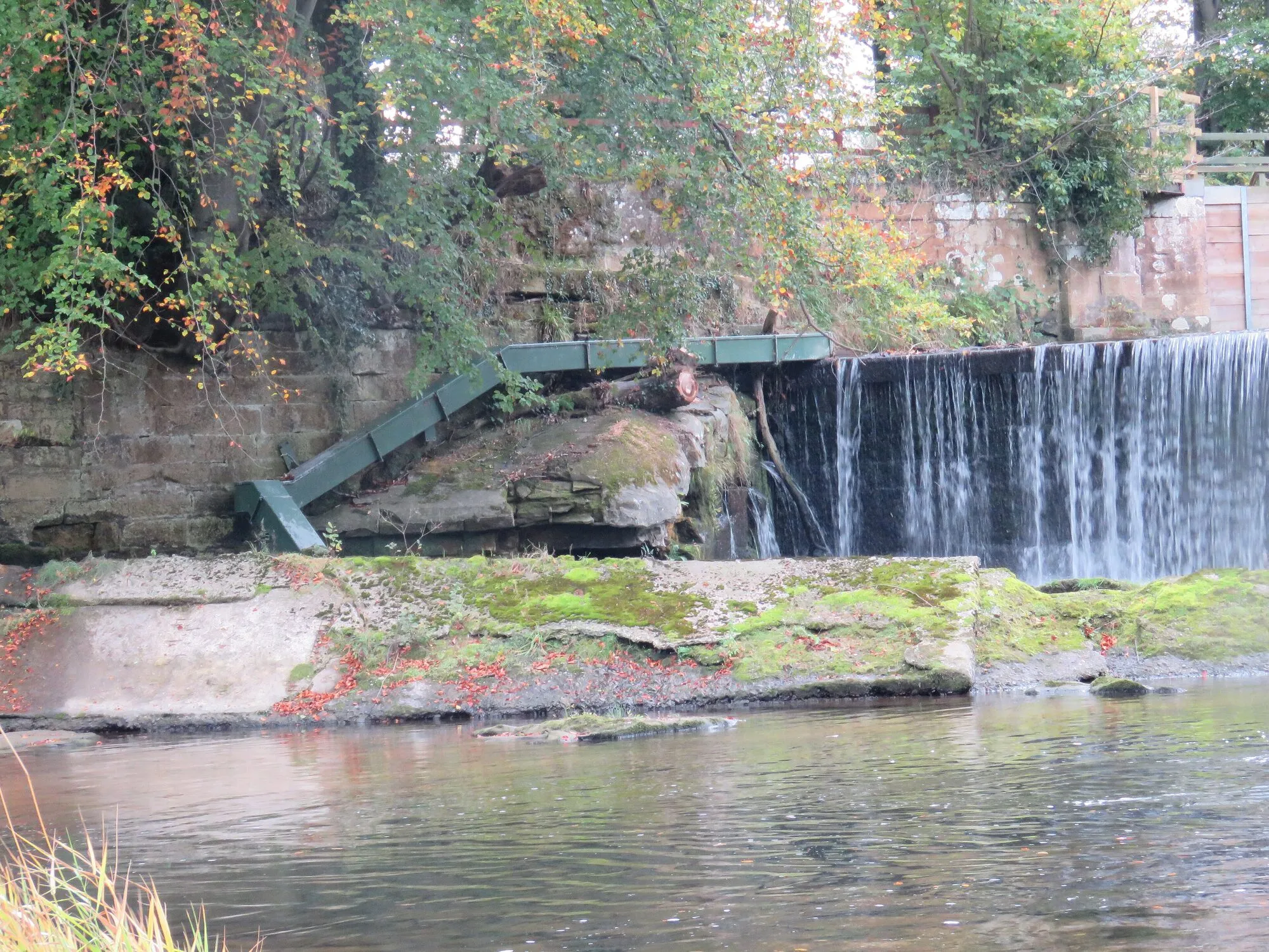 A stepped concrete fish pass running up beside a tall weir, with water pouring over the weir.