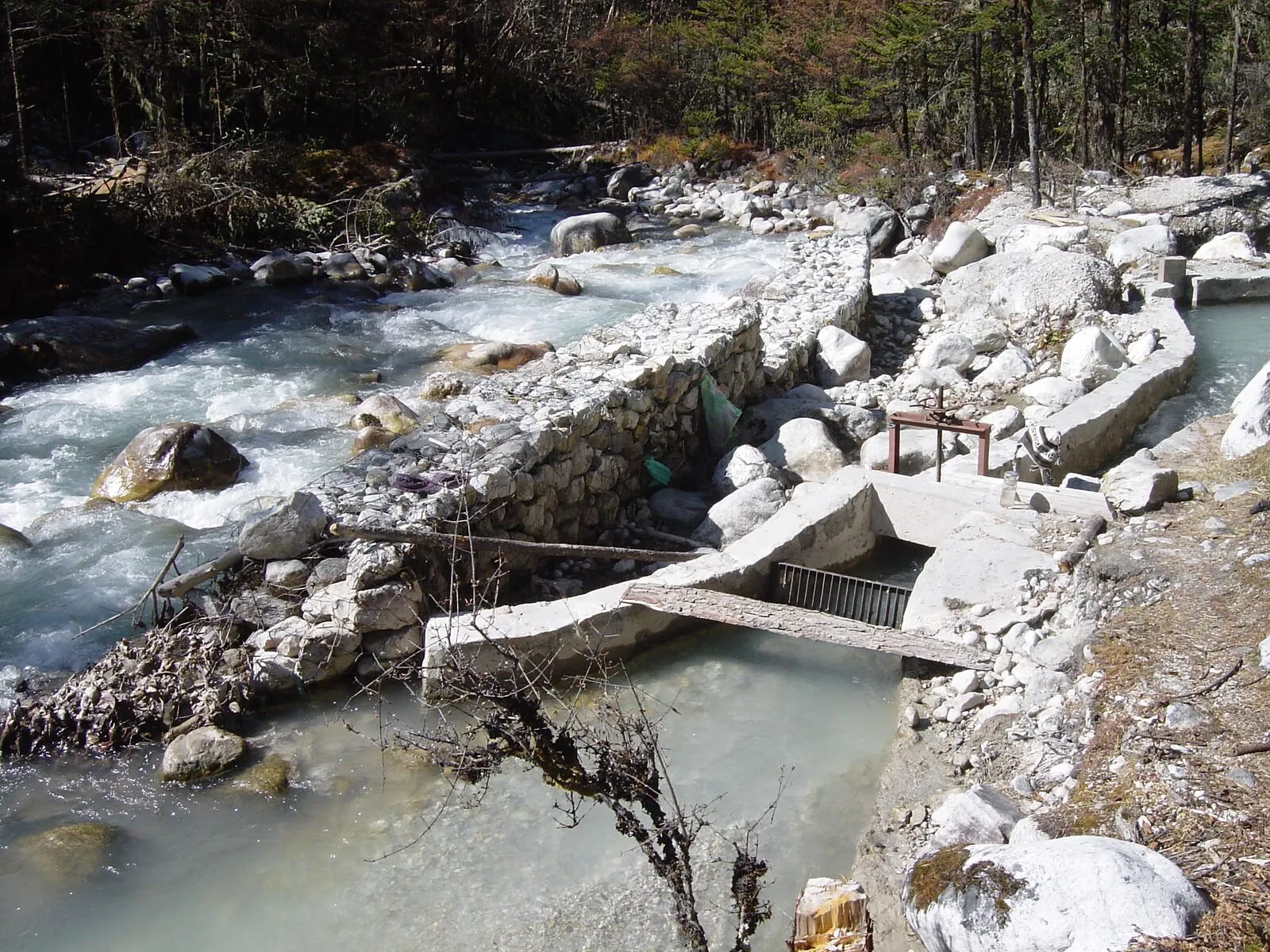A low stone weir across a rocky mountain river, with a concrete intake leading water off into a channel.