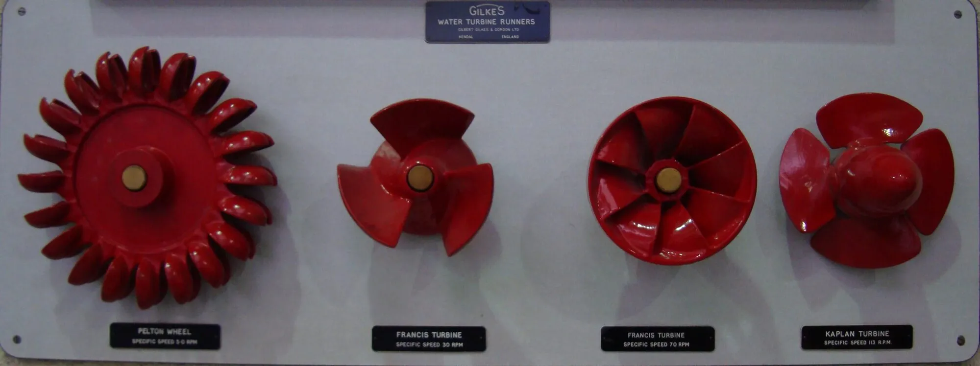 Four red turbine runners mounted in a row on a white display board.