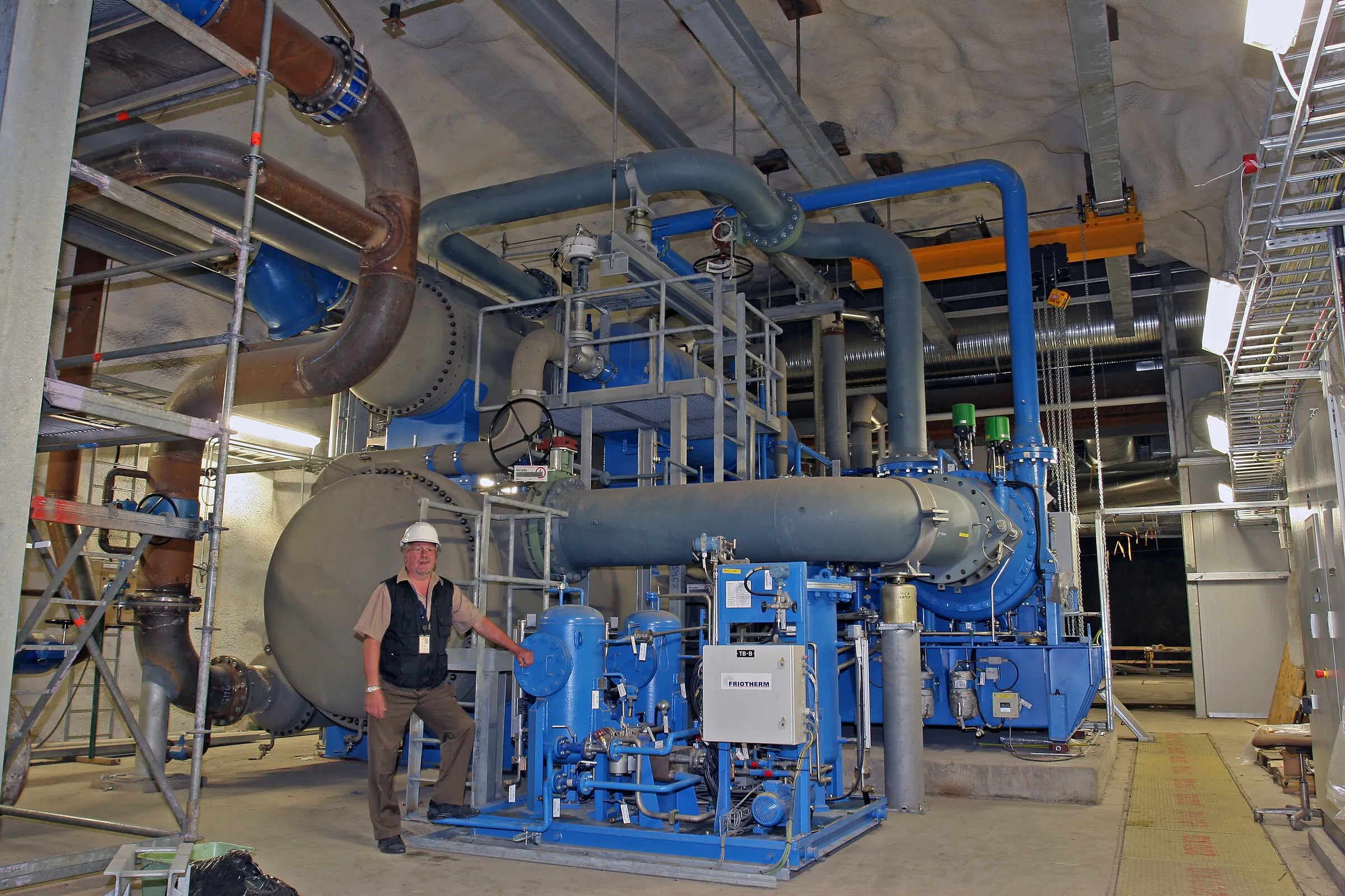 An engineer beside large blue heat pumps in the Katri Vala plant, a cavern under Helsinki that takes heat from treated wastewater.