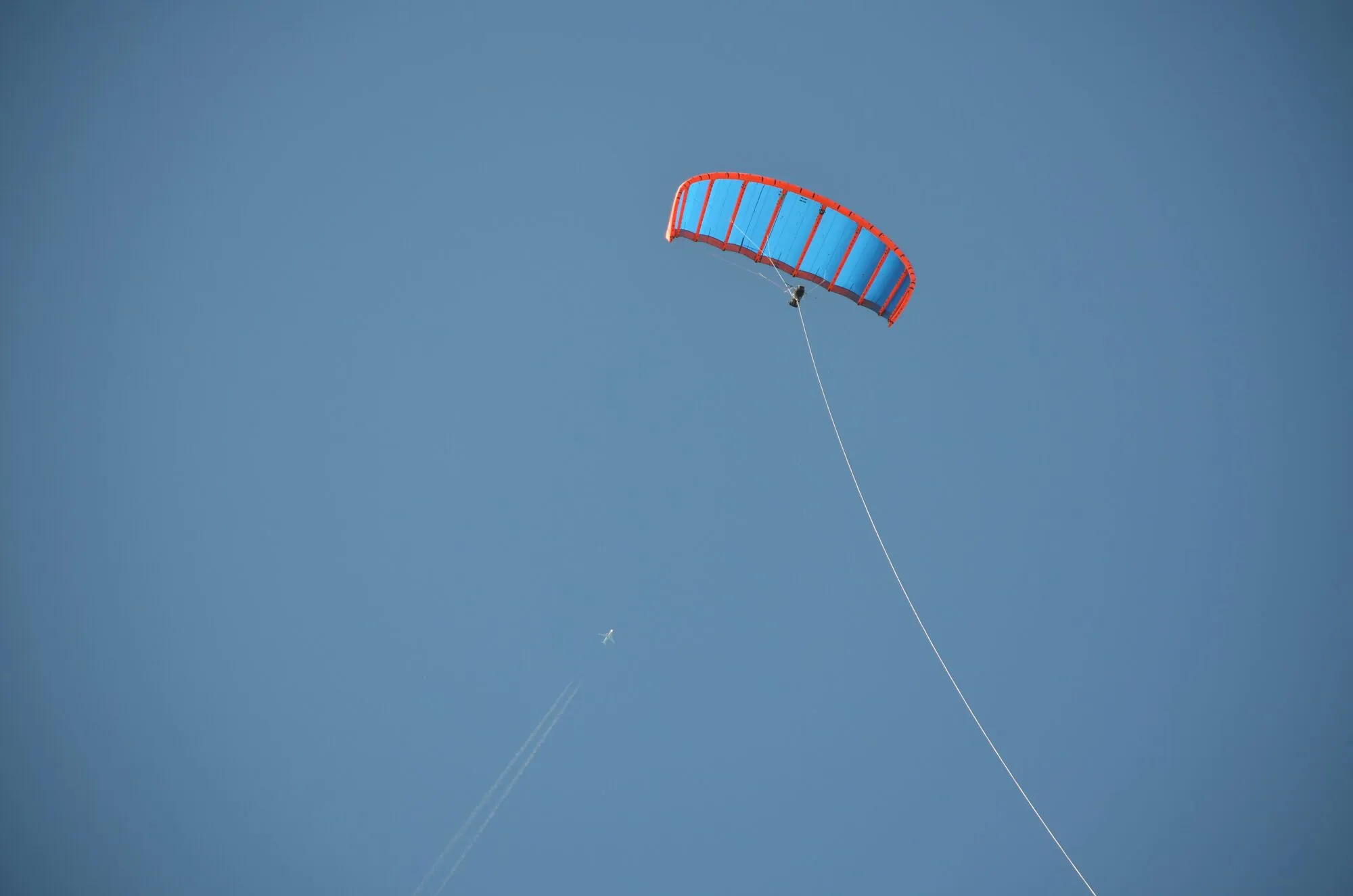A red and blue leading-edge inflatable kite flying high against a clear blue sky on a long thin tether.