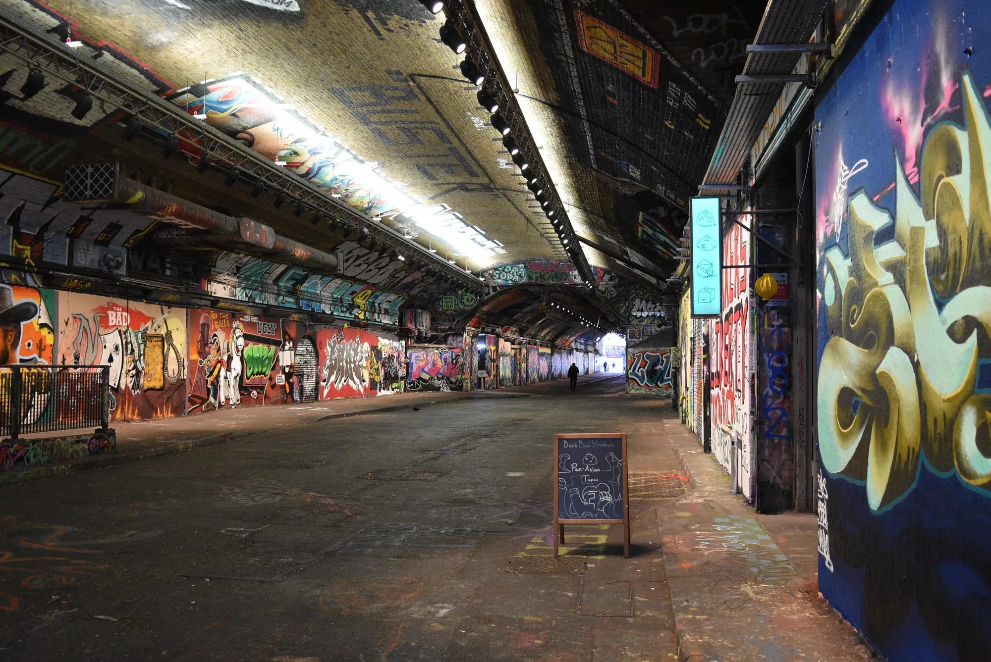 'n Lang straattunnel onder 'n spoorlyn, waarvan die mure en plafon van einde tot einde met kleurvolle geverfde stukkies bedek is.