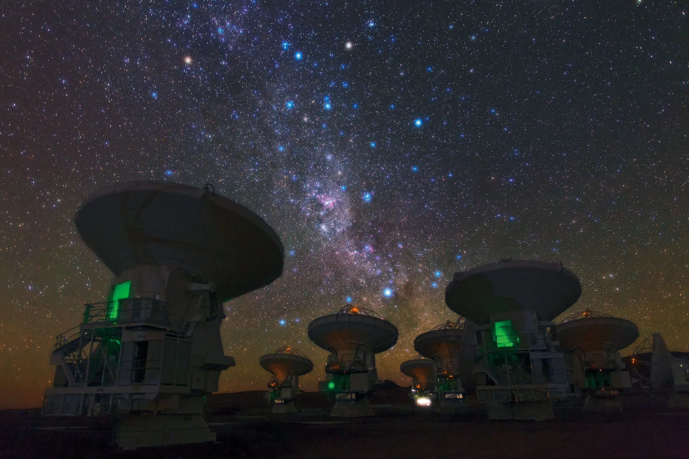 The Milky Way arching over radio telescope dishes in a desert night.