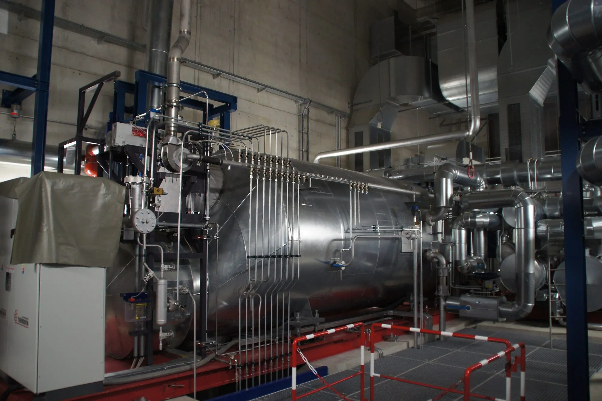 A large silver insulated vessel with pipework and valves: an organic Rankine cycle unit in an industrial hall.