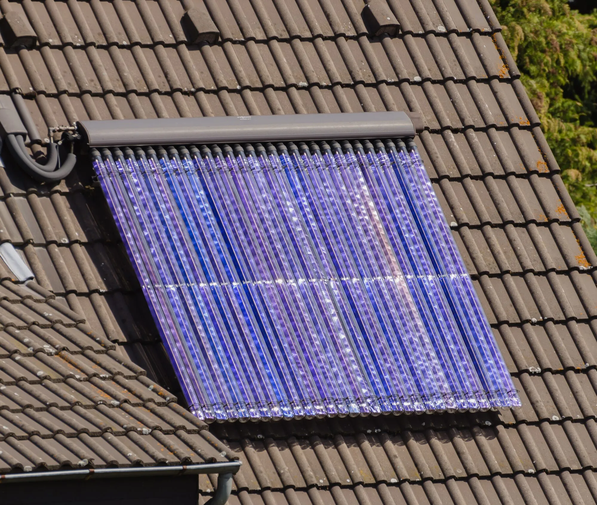 A solar thermal collector made of rows of glass tubes, mounted on a brown tiled roof.