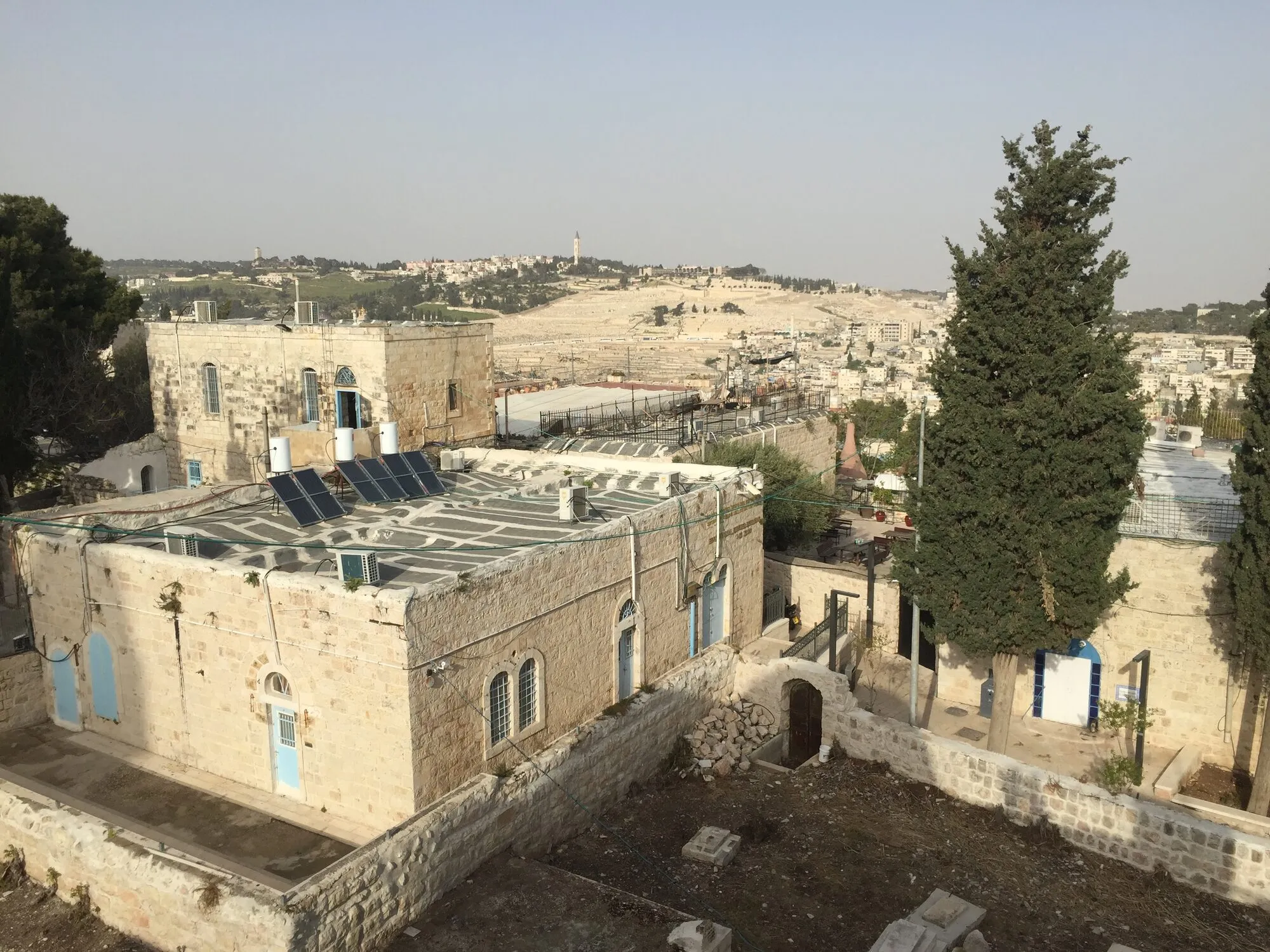 Old stone houses in Jerusalem with solar water heaters and tanks on their flat roofs, and the city stretching away behind.