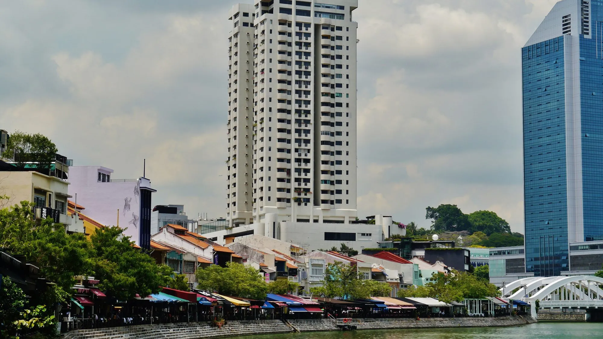 Colorful low shophouses of Boat Quay along the Singapore River, with office tower behind.