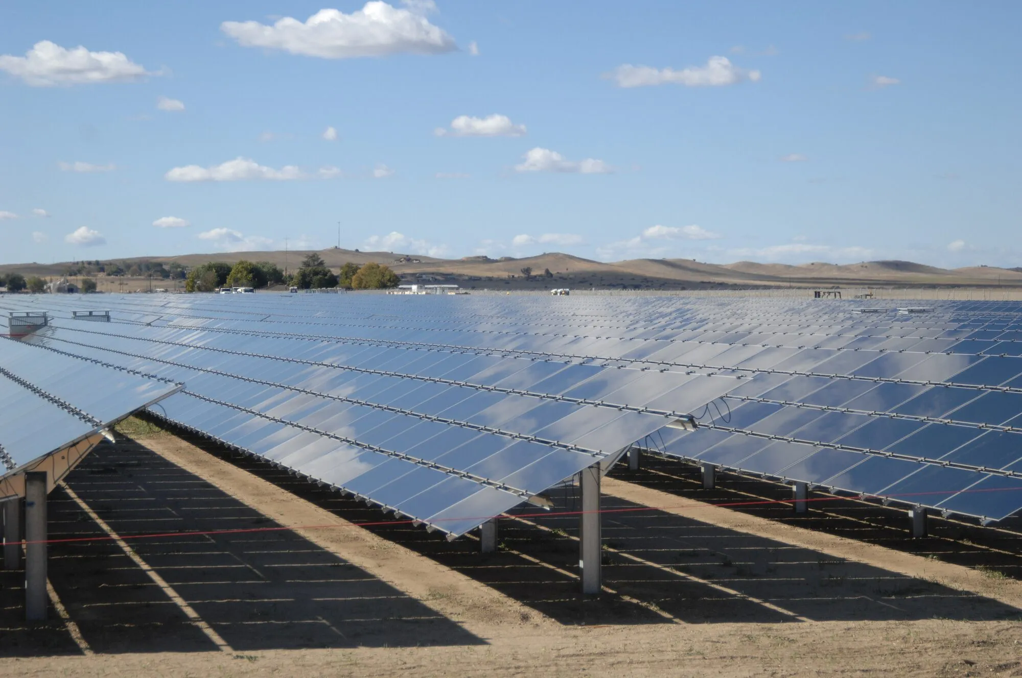 Long rows of solar panels on steel frames stretching across a dry Californian valley under a blue sky.