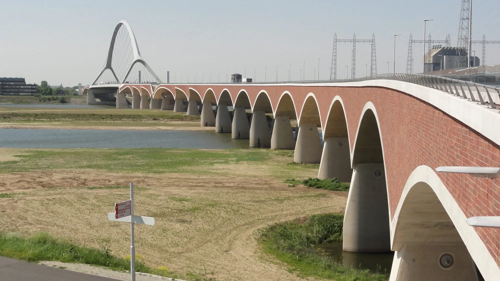 'n Lang baksteenboogbrug wat 'n nuwe kantkanaal van die rivier Waal by Nijmegen oorsteek, met 'n wit boogbrug in die verte.