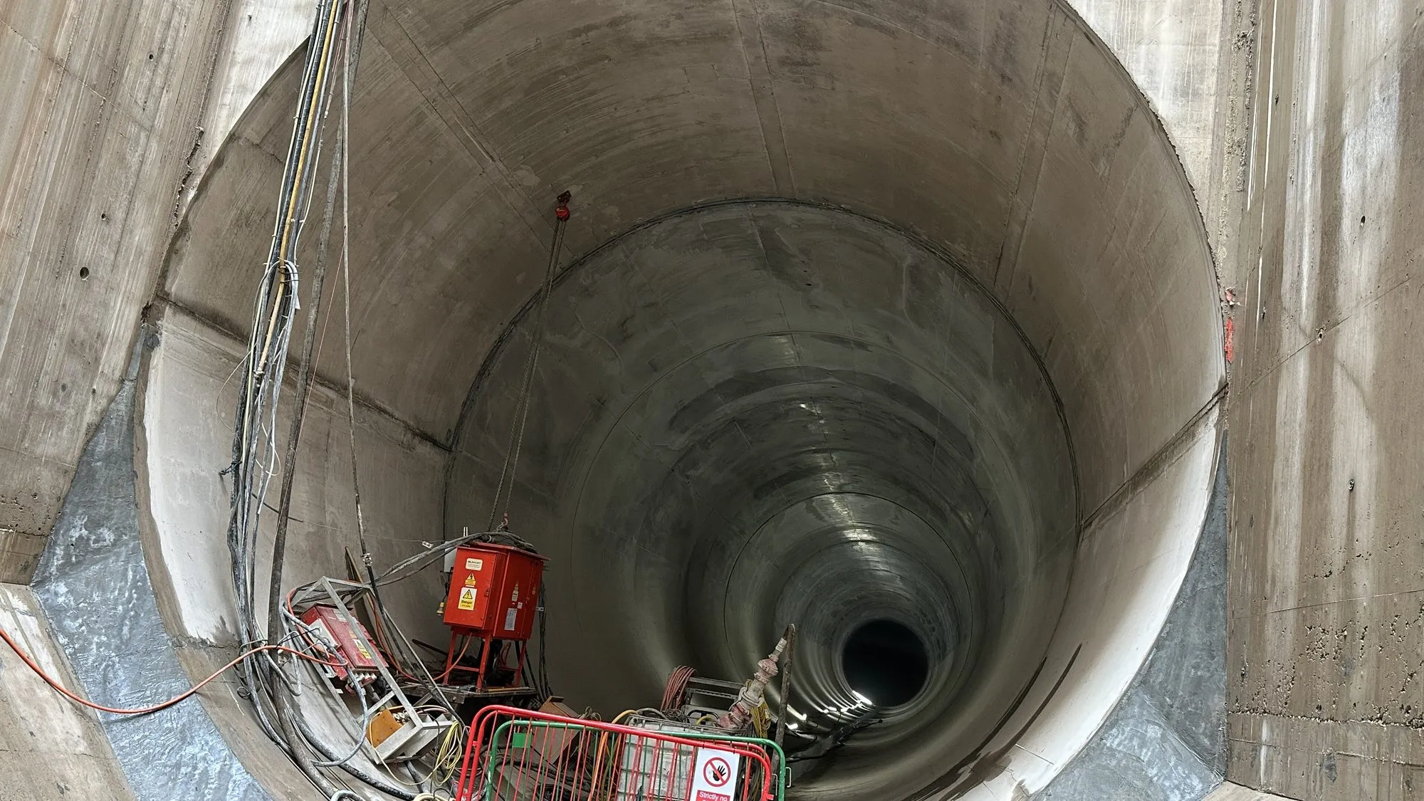 Looking down a deep circular concrete shaft of the Thames Tideway Tunnel, with a tunnel opening far below.