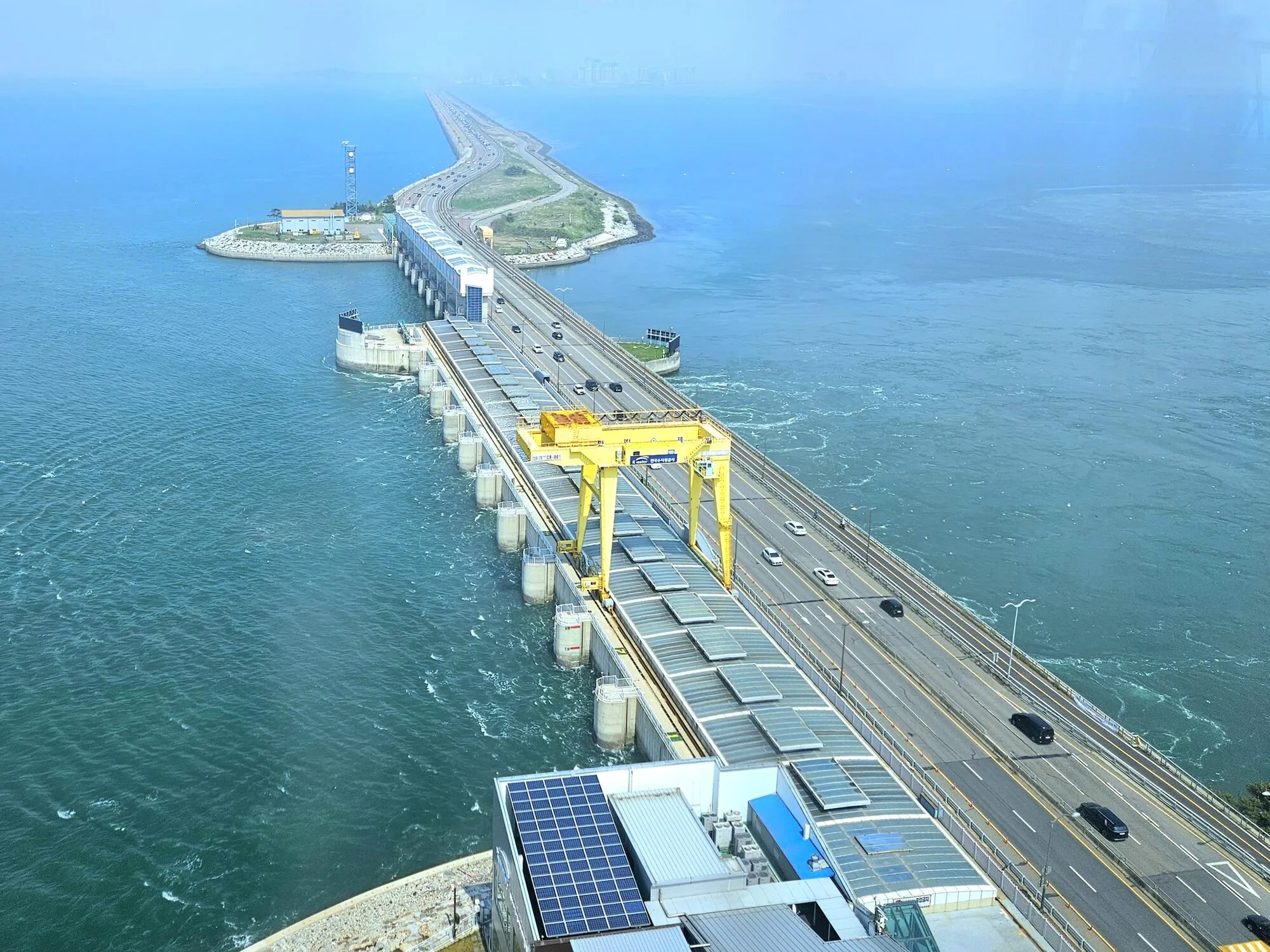 A power station built into a long sea wall with a road on top, the sea on one side and a lake on the other.