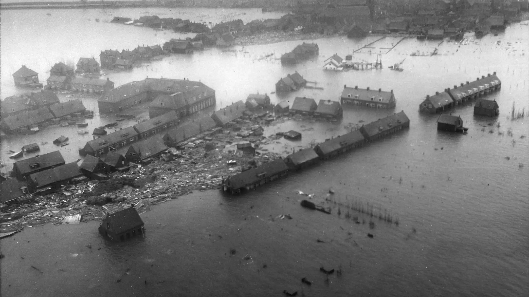 Swart-en-wit lugfoto van 'n Nederlandse dorp wat tot op die dak oorstroom is, met die strate in water verander.