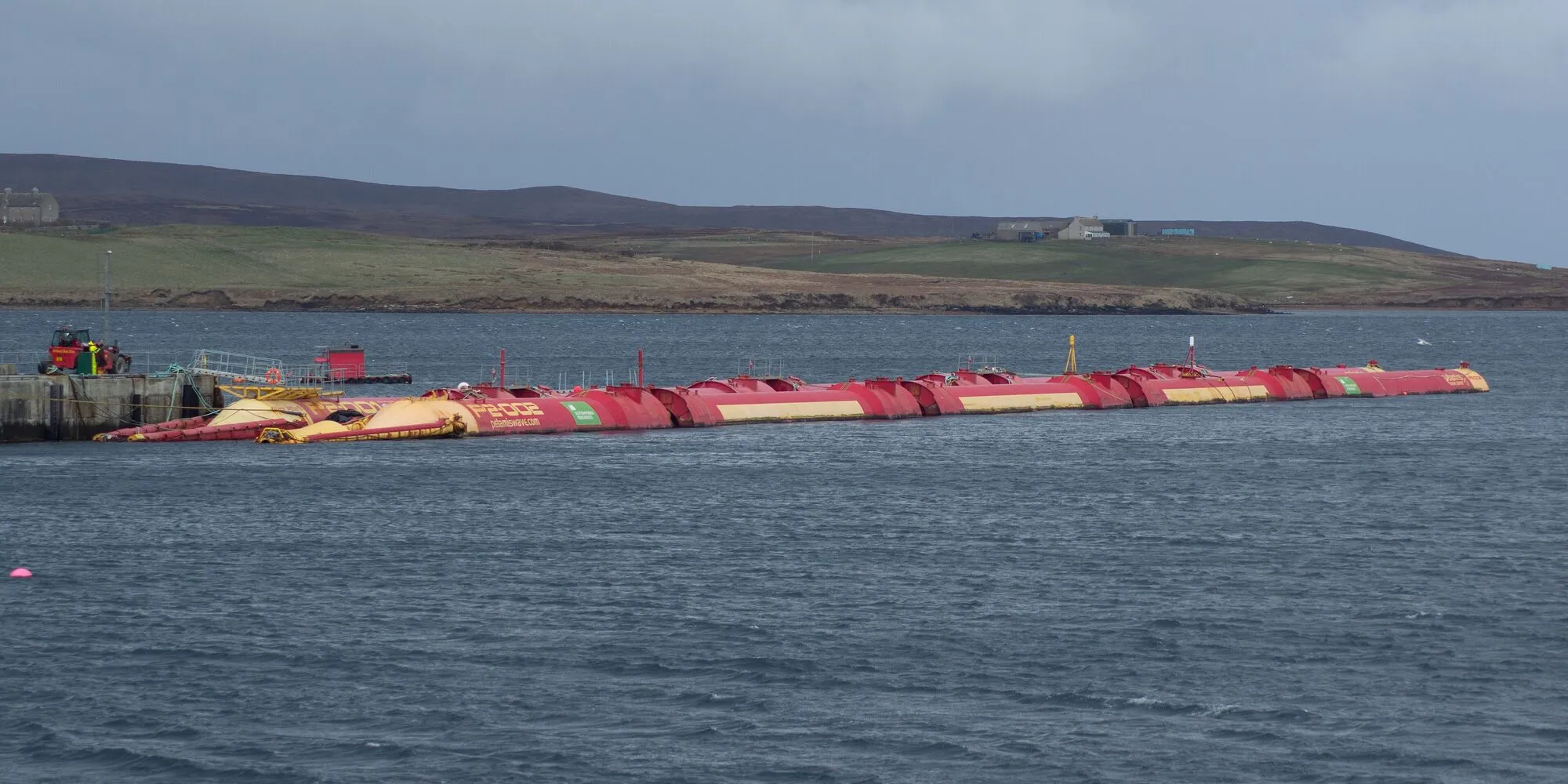 Two long red Pelamis wave machines lying at a quay in Orkney.