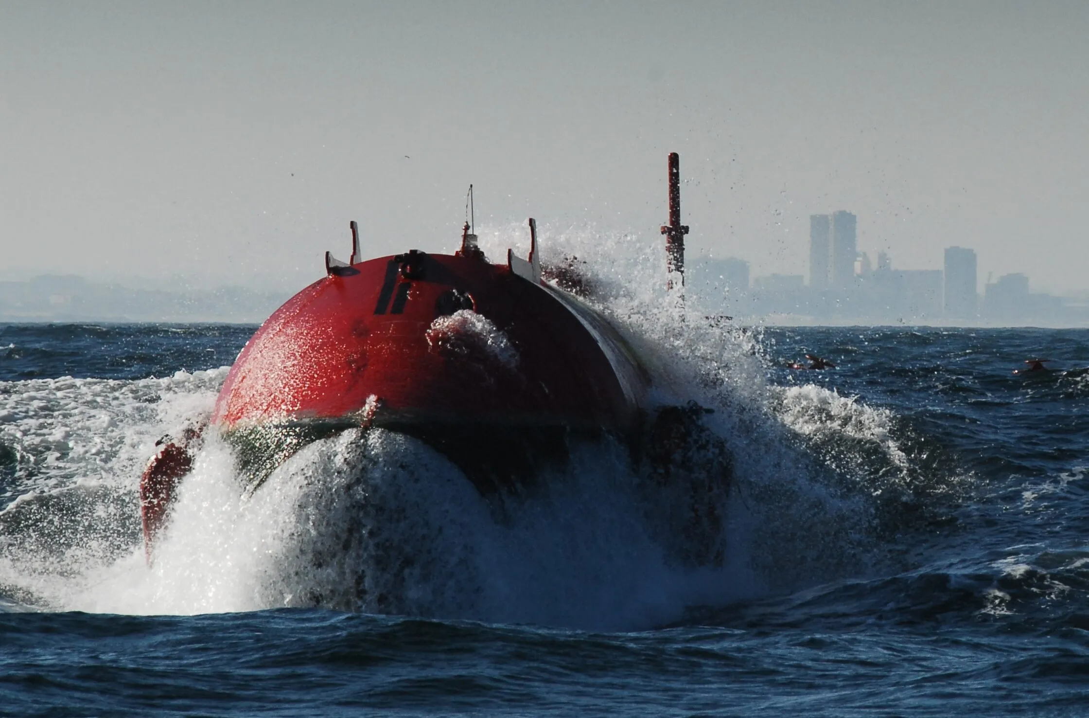 The red nose of a Pelamis wave energy machine bursting through a breaking wave, spray flying.